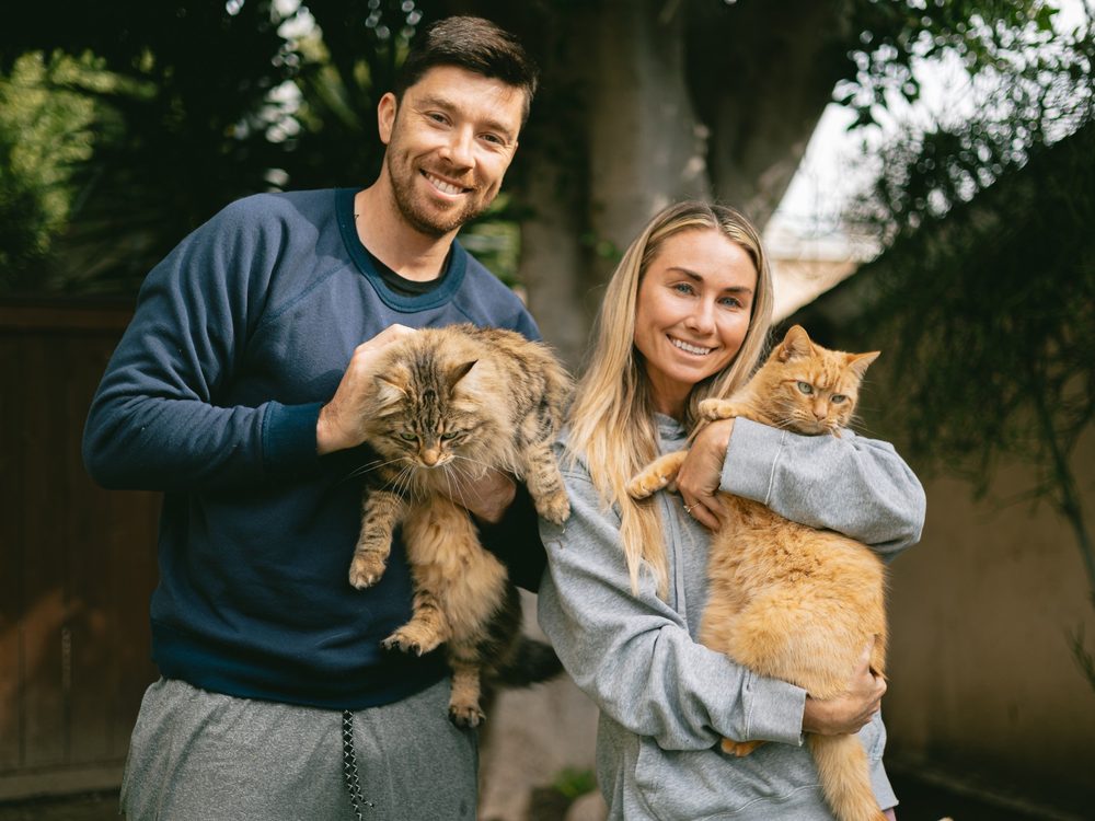 Chris and Lauren smiling in their backyard, each holding one of their two cats
